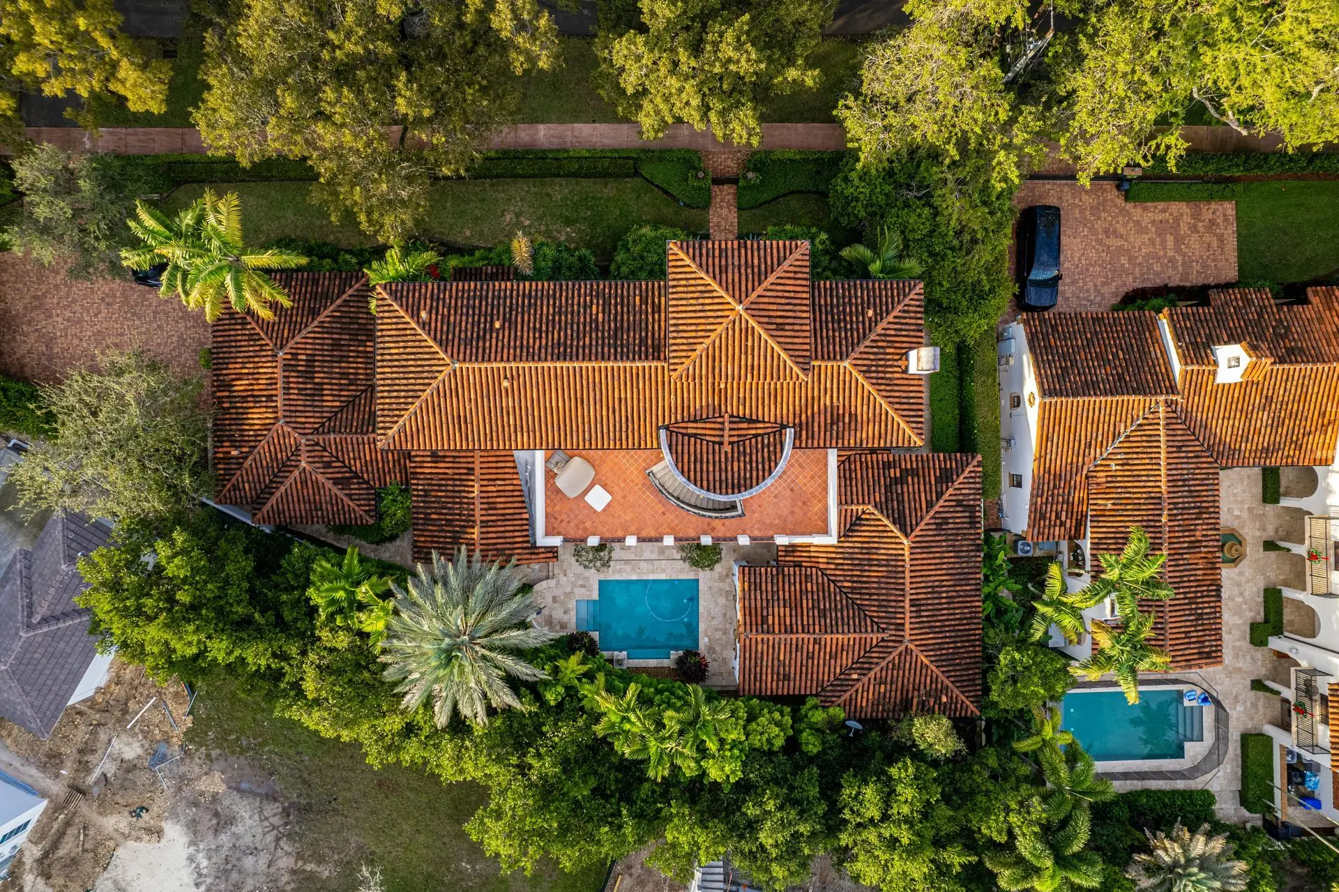 Aerial view of a house with a tile roof, pool, and surrounding trees.