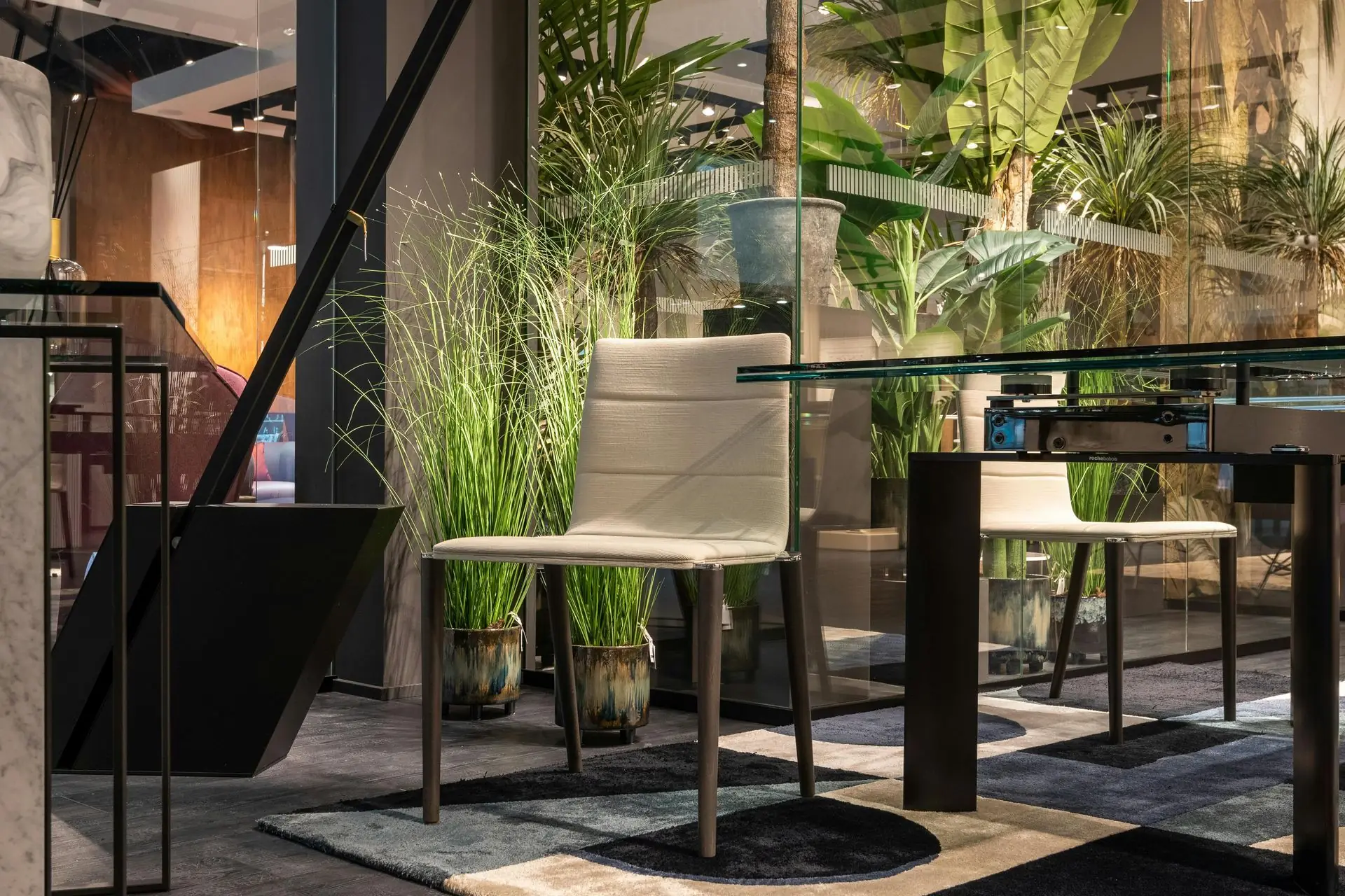 A modern interior with a chair, glass table, and plants. Neutral tones and natural light.
