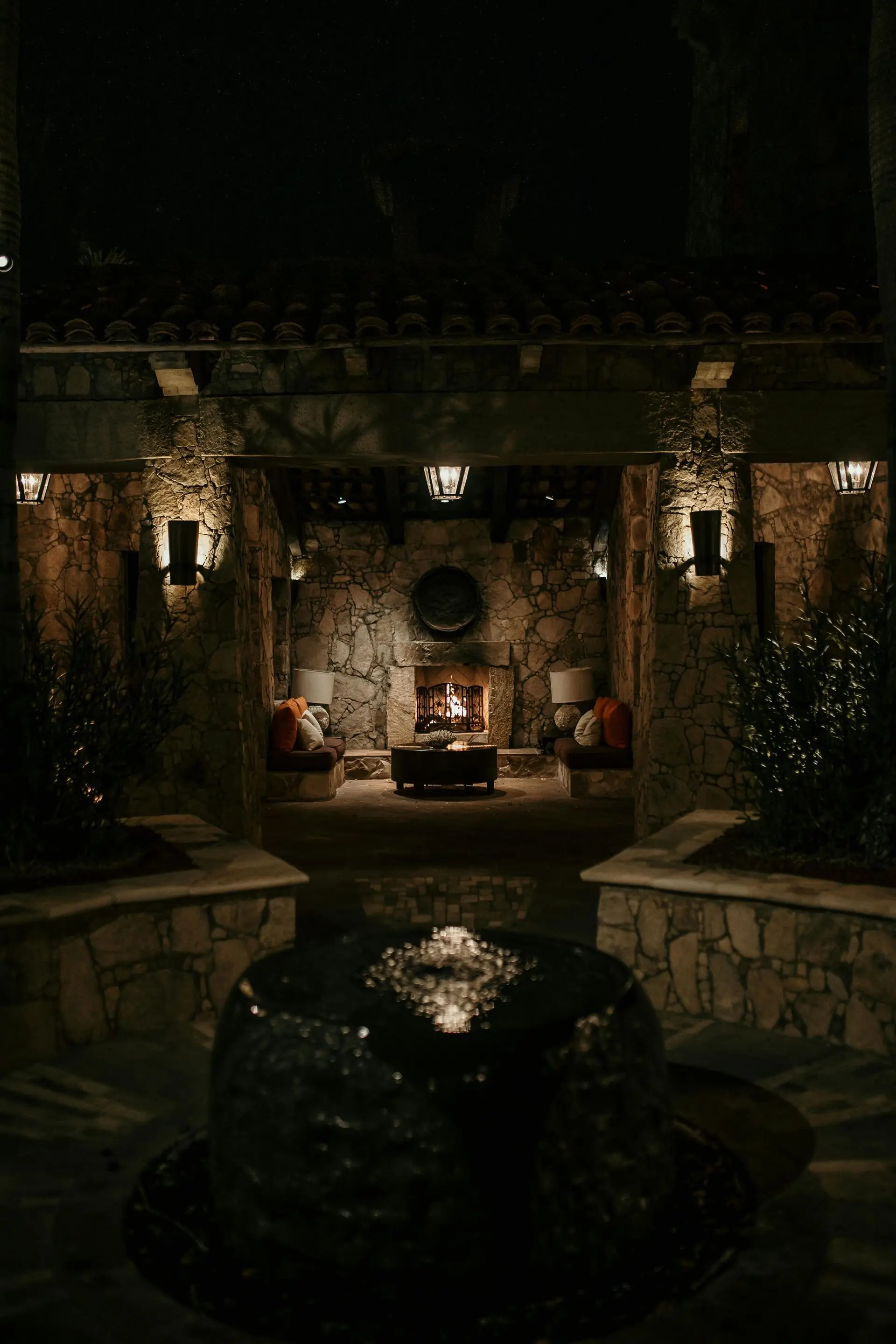 Outdoor patio lounge lit at night with warm ambient lighting and tropical planting.