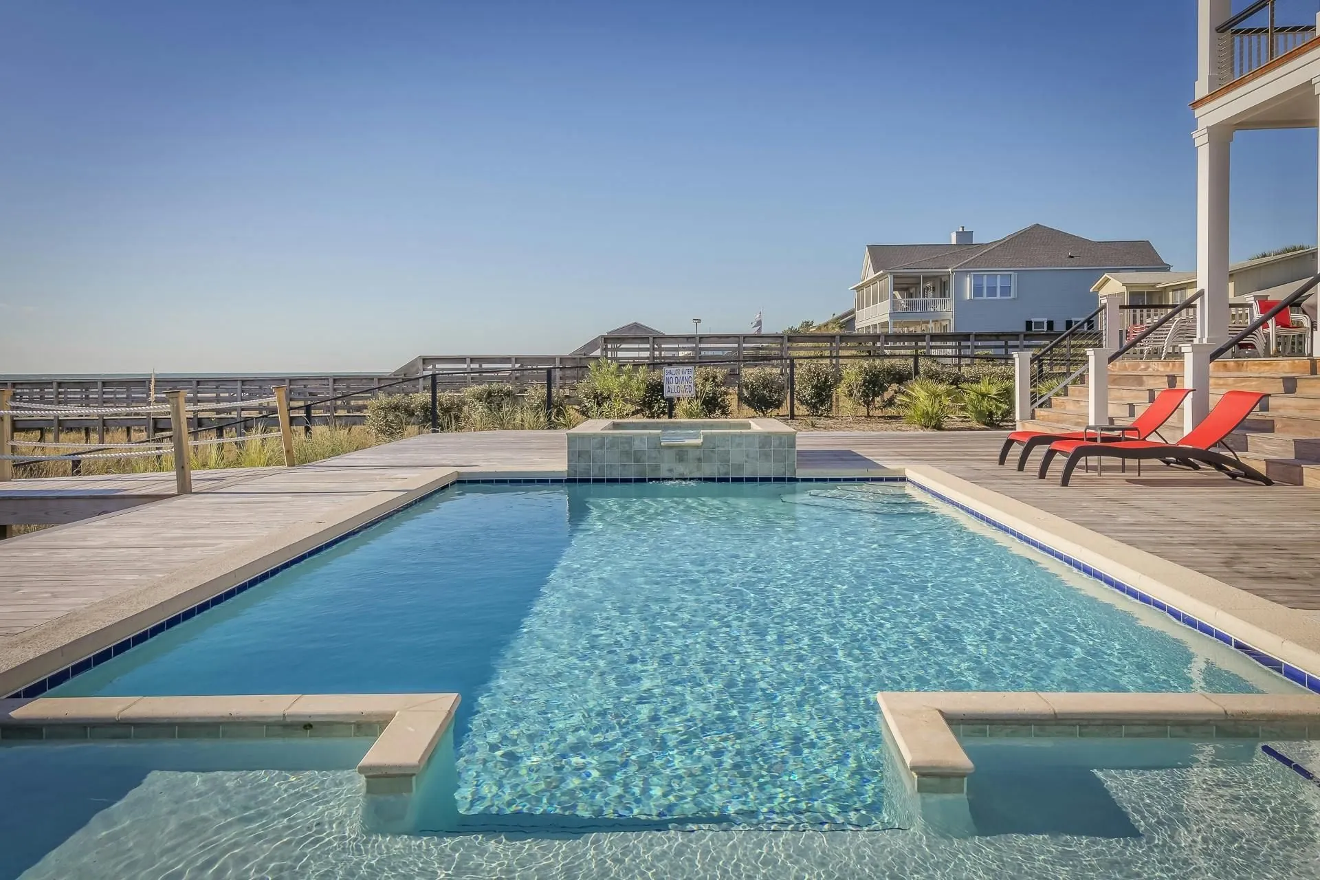 Swimming pool next to a house with blue sky. Lounge chairs, a pergola and steps are visible.